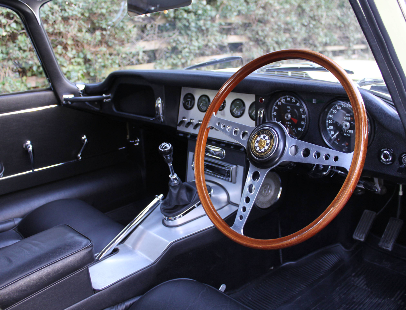 Interior of a right-hand-drive Series 1 E-Type showing the aluminium dash panel, toggle switches, wood-rimmed steering wheel and centre console